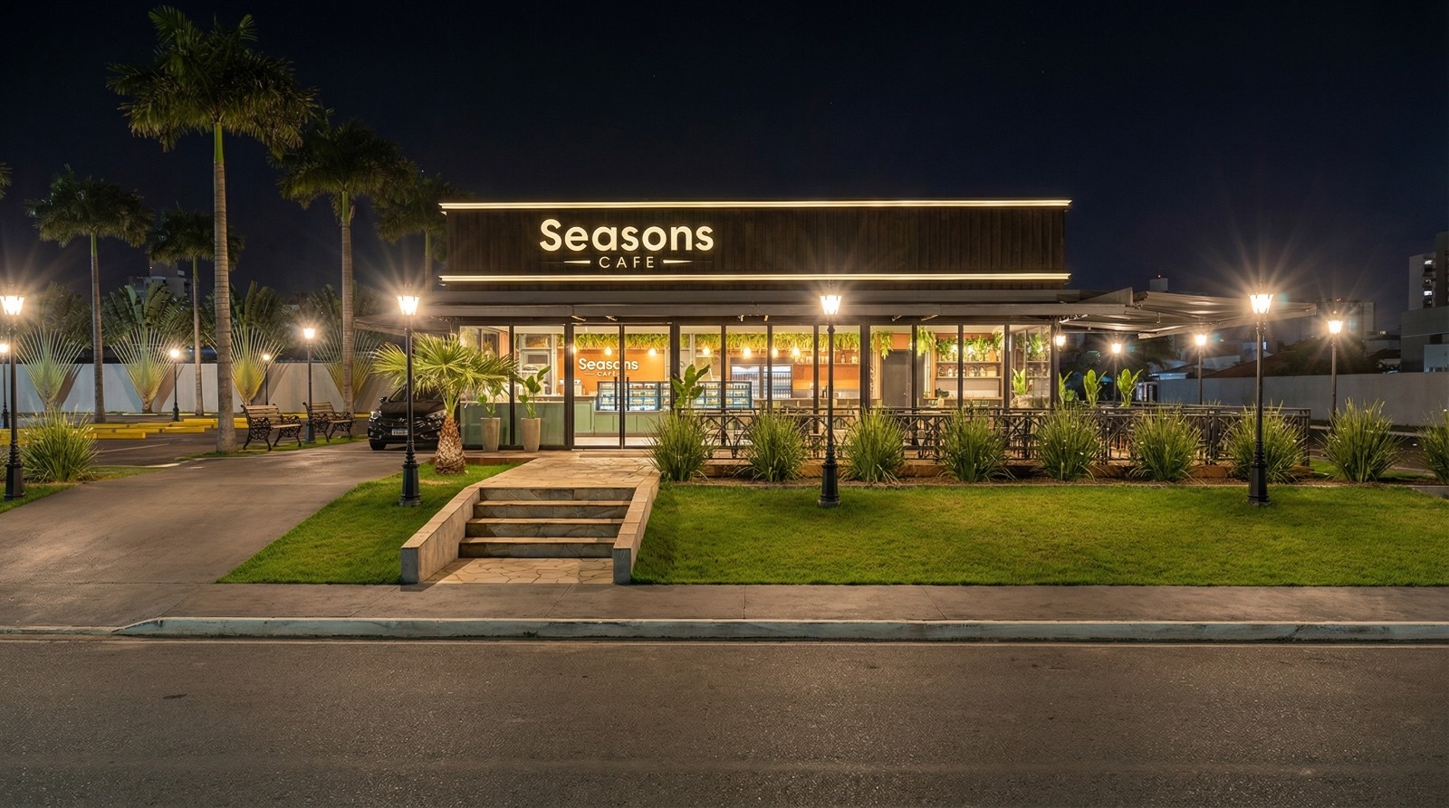 Fachada iluminada do Seasons Café à noite, com palmeiras, jardim e escada de entrada